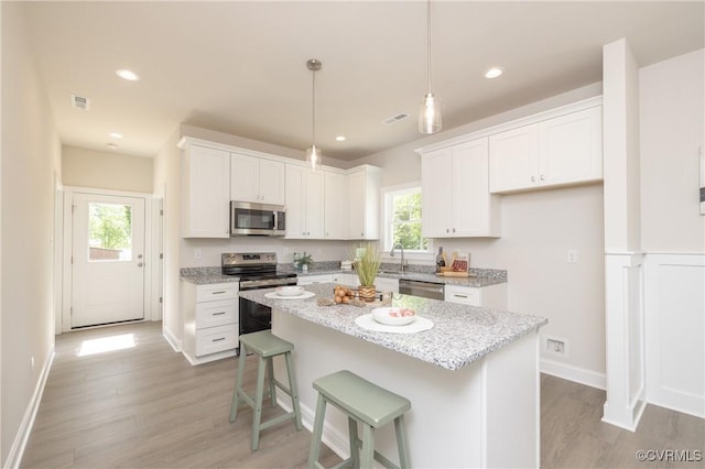 kitchen featuring appliances with stainless steel finishes, light wood-style floors, white cabinets, a center island, and pendant lighting