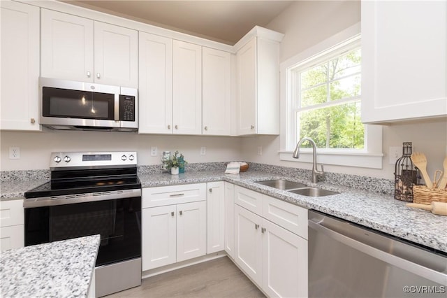 kitchen featuring appliances with stainless steel finishes, a sink, white cabinets, and light stone countertops