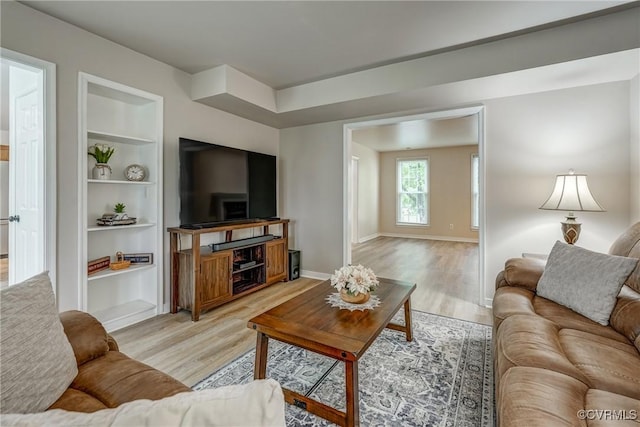 living room featuring built in shelves, light wood-style flooring, and baseboards