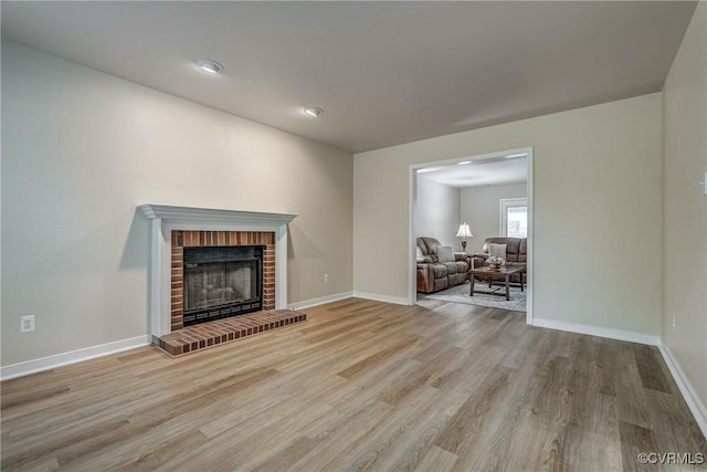 living room with wood finished floors, a brick fireplace, and baseboards