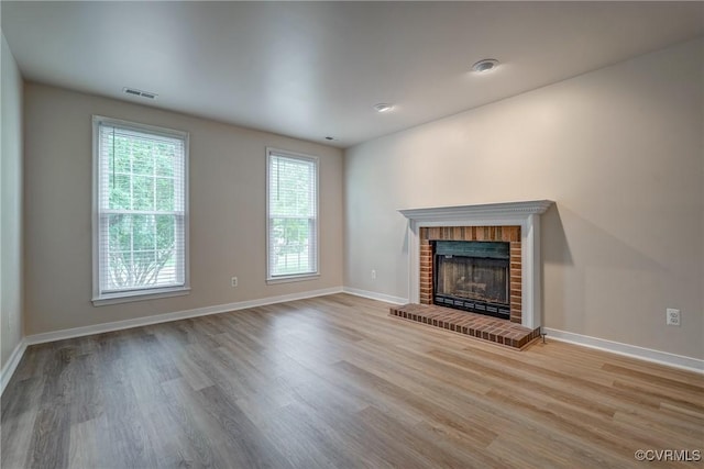 unfurnished living room with wood finished floors, a brick fireplace, and baseboards