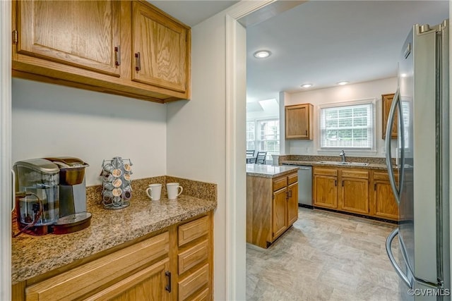 kitchen with appliances with stainless steel finishes, a sink, brown cabinetry, and light stone counters