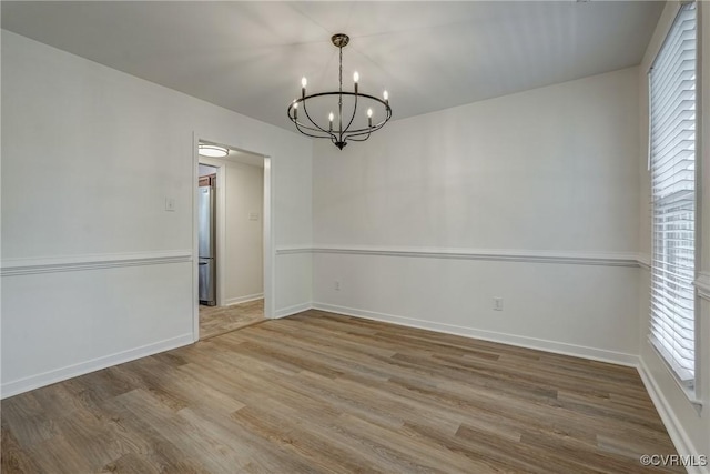 unfurnished room featuring wood finished floors, a chandelier, healthy amount of natural light, and baseboards