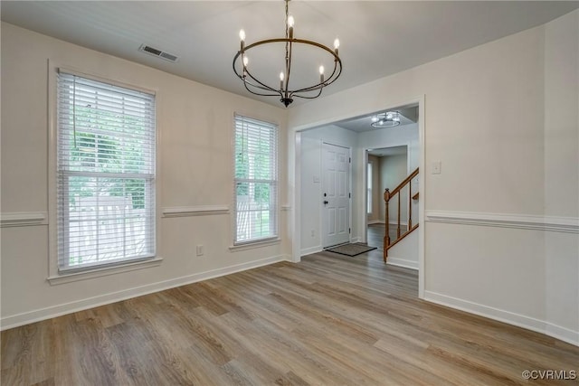 unfurnished dining area with a chandelier, light wood-style floors, stairway, and baseboards
