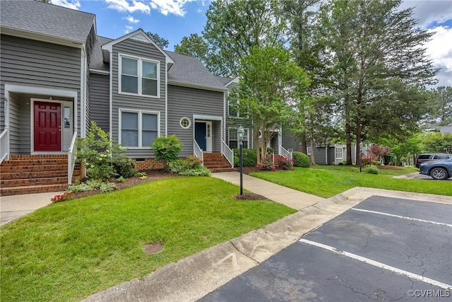 townhome / multi-family property featuring a front lawn, entry steps, a shingled roof, and uncovered parking