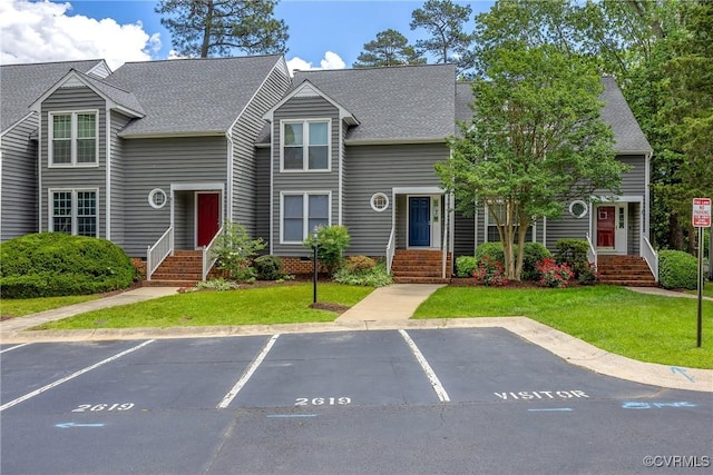 view of property with uncovered parking, a shingled roof, and a front lawn