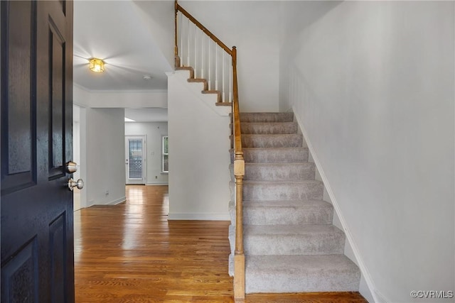 staircase featuring wood finished floors, baseboards, and ornamental molding