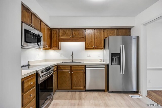 kitchen featuring appliances with stainless steel finishes, a sink, light countertops, light wood-type flooring, and brown cabinets