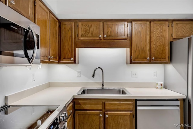 kitchen with appliances with stainless steel finishes, a sink, light countertops, and brown cabinets