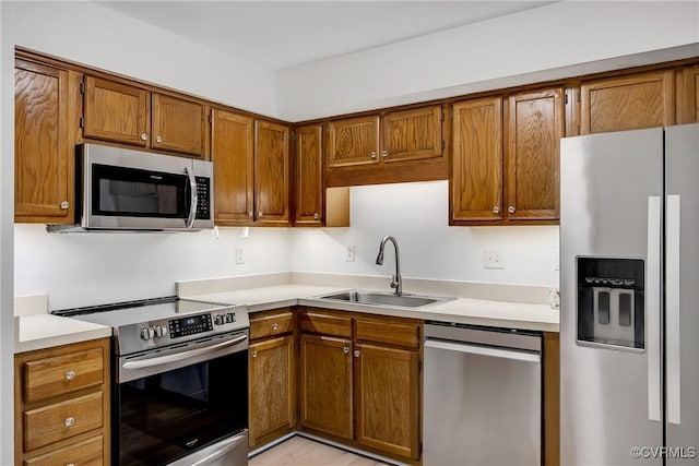 kitchen with appliances with stainless steel finishes, a sink, brown cabinets, and light countertops