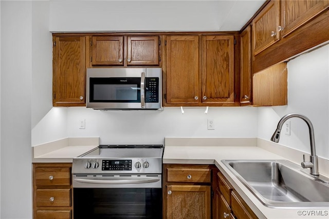 kitchen with appliances with stainless steel finishes, a sink, light countertops, and brown cabinetry