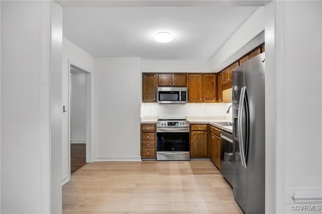 kitchen with stainless steel appliances, light wood-type flooring, a sink, and light countertops