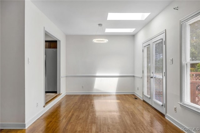 empty room with a skylight, wood finished floors, and baseboards