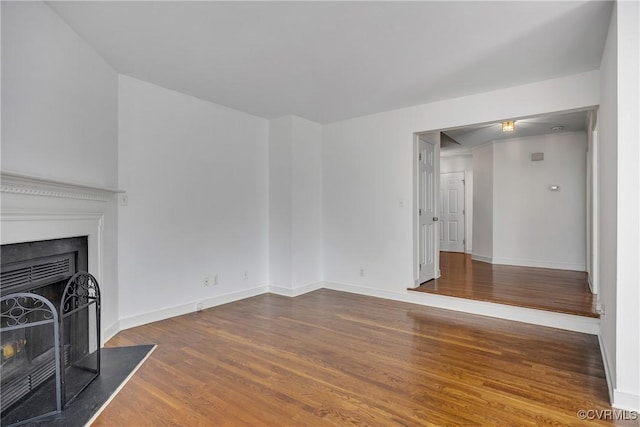 unfurnished living room with wood finished floors, baseboards, and a fireplace with flush hearth