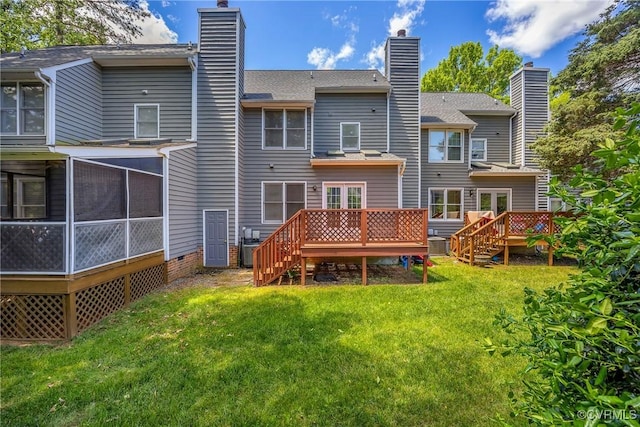 rear view of property featuring a chimney, a deck, a lawn, and a sunroom