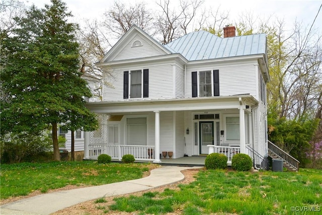 view of front of house with a chimney, a standing seam roof, covered porch, metal roof, and a front lawn