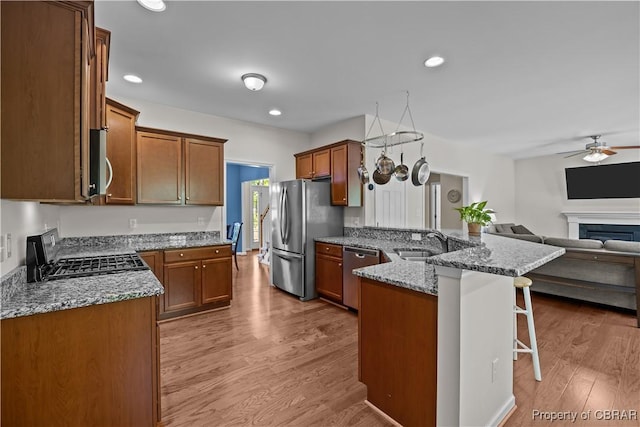 kitchen featuring stainless steel appliances, a kitchen bar, a peninsula, light stone countertops, and open floor plan