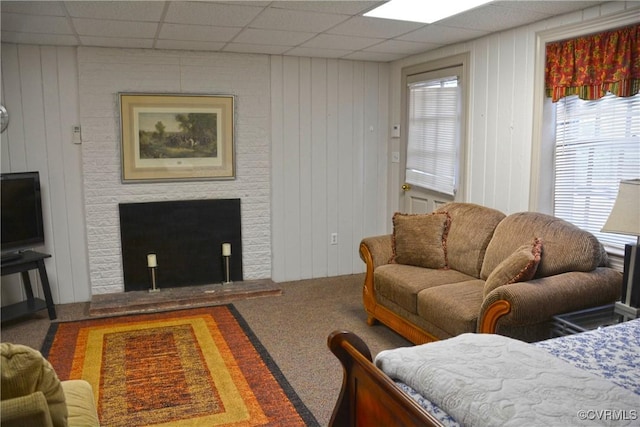 living area featuring a fireplace, a drop ceiling, carpet, and wood walls