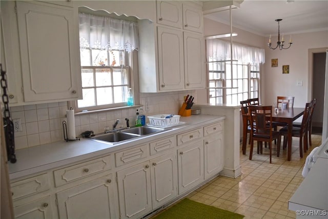 kitchen featuring a sink, white cabinets, crown molding, tasteful backsplash, and a chandelier