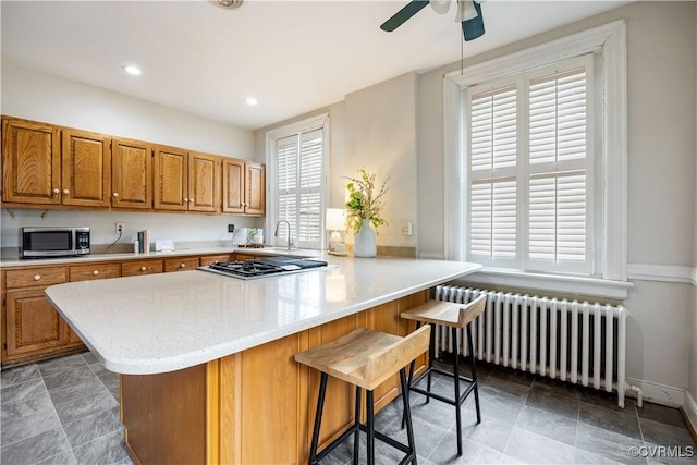 2706 W Grace St, Richmond, VA 23220 - kitchen featuring radiator, appliances with stainless steel finishes, ceiling fan, a kitchen breakfast bar, and brown cabinetry