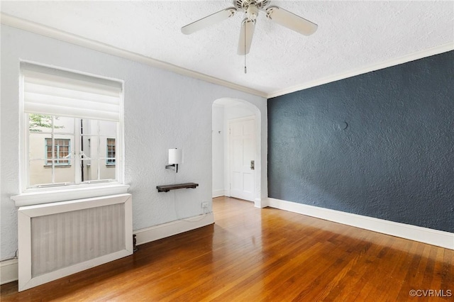 empty room with a textured wall, wood finished floors, radiator heating unit, a textured ceiling, and arched walkways