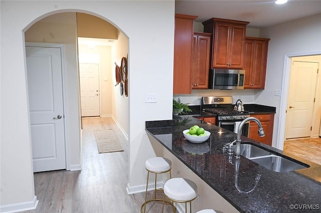 5801 Riverside Trl, Richmond, VA 23225 - kitchen with stainless steel appliances, a sink, dark stone countertops, light wood-style flooring, and arched walkways