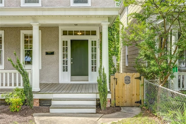 entrance to property with covered porch, stucco siding, and fence