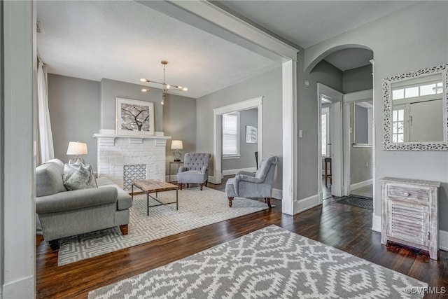 living area with arched walkways, wood finished floors, baseboards, a chandelier, and a brick fireplace