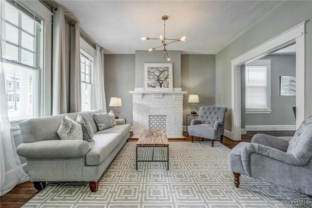 living room with wood finished floors, a chandelier, baseboards, a brick fireplace, and a textured ceiling