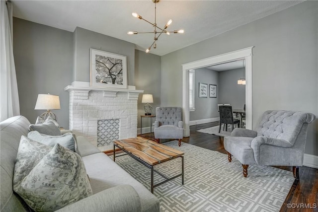 living area featuring a chandelier, wood finished floors, baseboards, and a brick fireplace