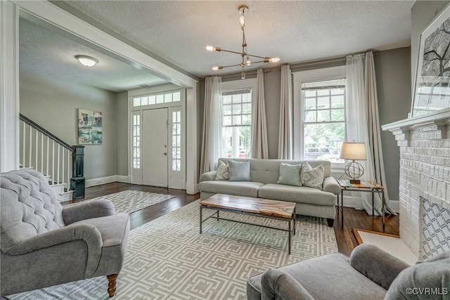 living area featuring a textured ceiling, a chandelier, stairway, a brick fireplace, and wood finished floors