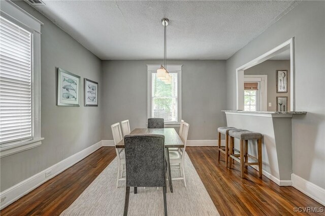 dining room with dark wood finished floors, a textured ceiling, and baseboards