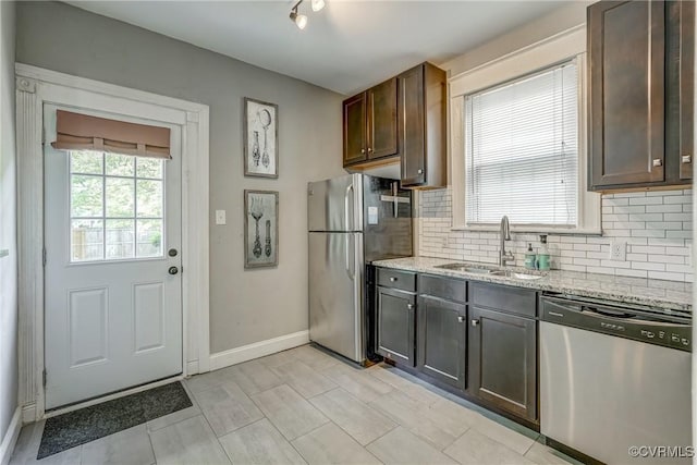 kitchen featuring stainless steel appliances, a sink, tasteful backsplash, baseboards, and light stone countertops