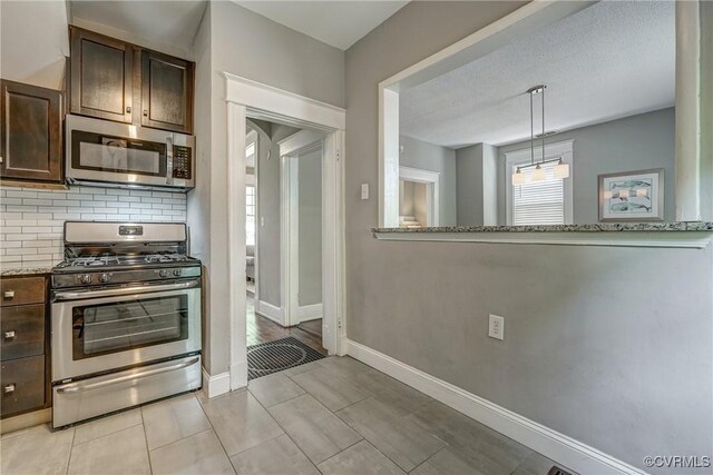 kitchen with appliances with stainless steel finishes, backsplash, dark brown cabinetry, baseboards, and light tile patterned flooring
