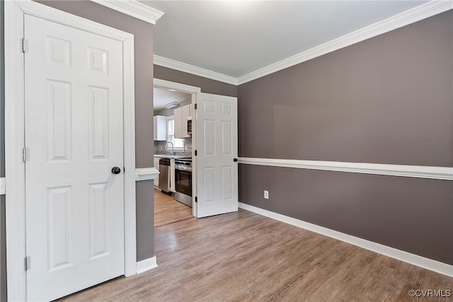 unfurnished room with light wood finished floors, baseboards, crown molding, and a sink