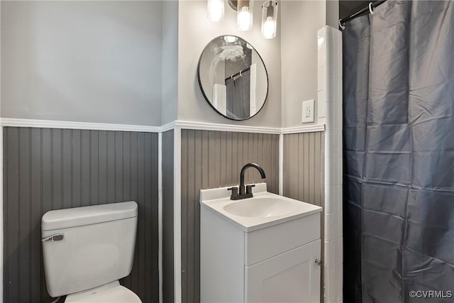 bathroom with a wainscoted wall, vanity, toilet, and curtained shower