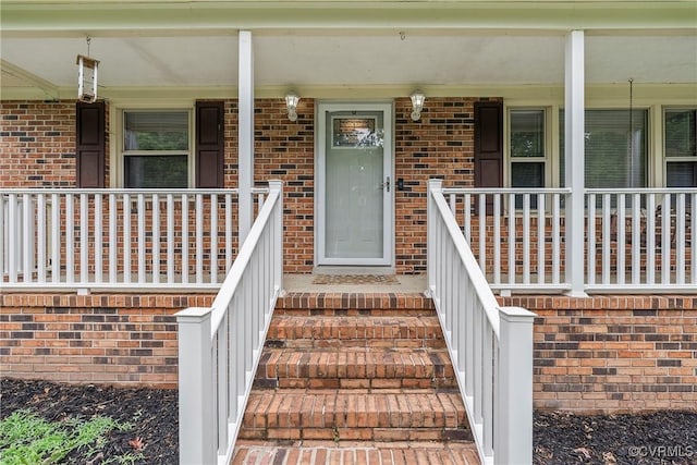 view of exterior entry featuring a porch and brick siding
