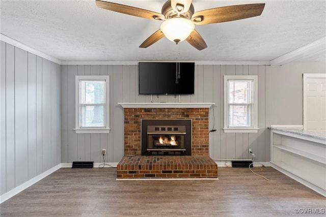 living room featuring ornamental molding, wood finished floors, a brick fireplace, a textured ceiling, and baseboards