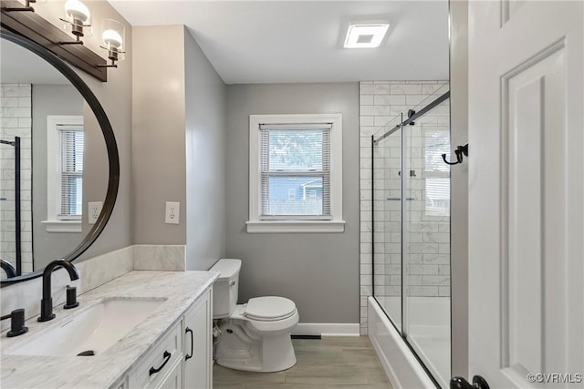 bathroom with toilet, baseboards, wood finished floors, vanity, and bath / shower combo with glass door