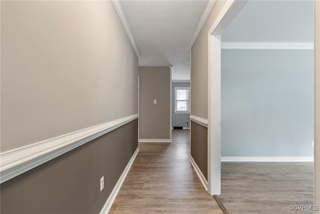 hallway with crown molding, wood finished floors, a textured ceiling, and baseboards