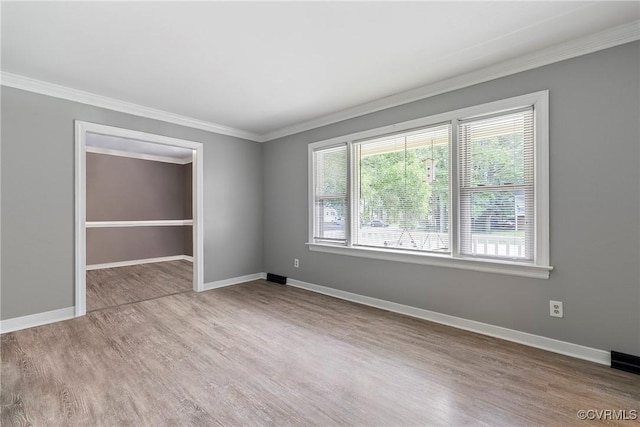 empty room with wood finished floors, ornamental molding, and baseboards