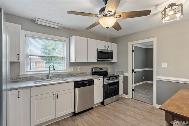 kitchen featuring stainless steel appliances, a sink, white cabinetry, light wood finished floors, and light stone counters