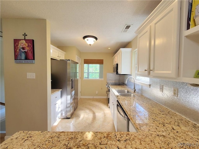 kitchen featuring appliances with stainless steel finishes, a sink, white cabinetry, backsplash, and a textured ceiling