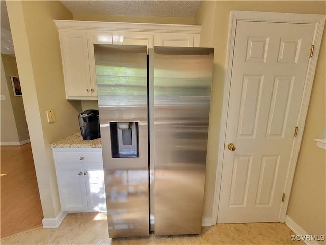 kitchen featuring stainless steel fridge with ice dispenser, baseboards, and white cabinetry