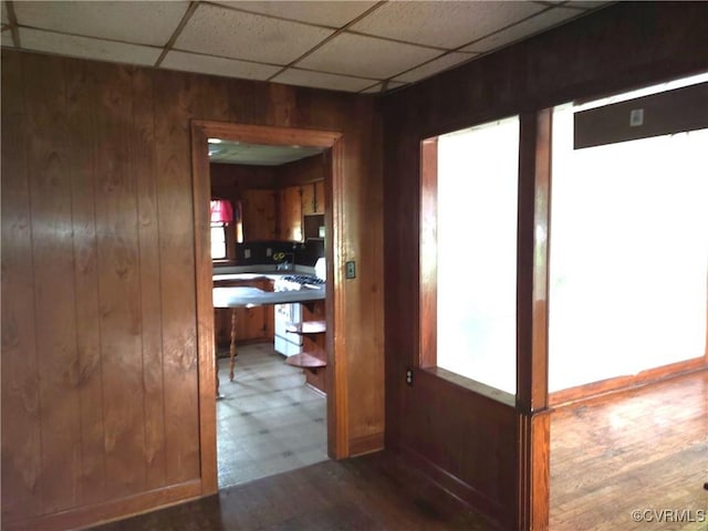 corridor featuring wooden walls, a drop ceiling, and wood finished floors