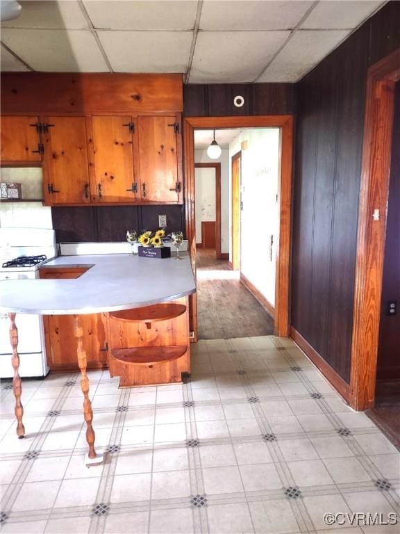 kitchen with white range with gas stovetop, light floors, wood walls, brown cabinets, and light countertops