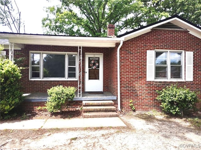 doorway to property with a chimney and brick siding