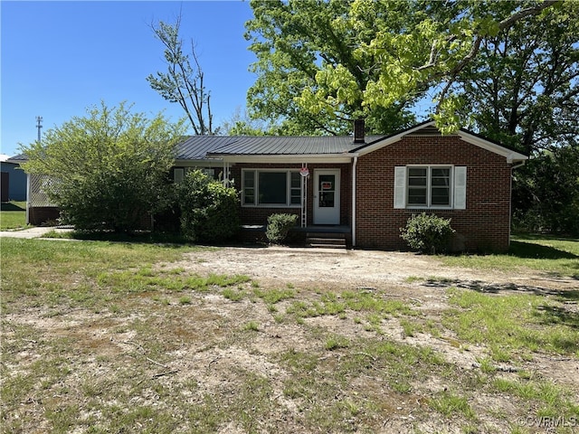 view of front of home featuring brick siding, a chimney, and metal roof