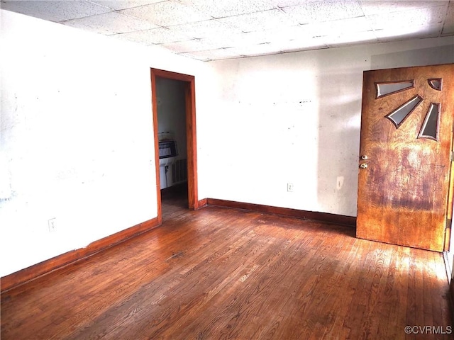 empty room featuring baseboards, wood-type flooring, and a paneled ceiling