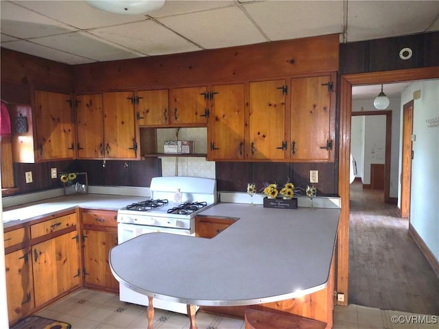 kitchen with brown cabinets, light countertops, white range with gas stovetop, a peninsula, and open shelves